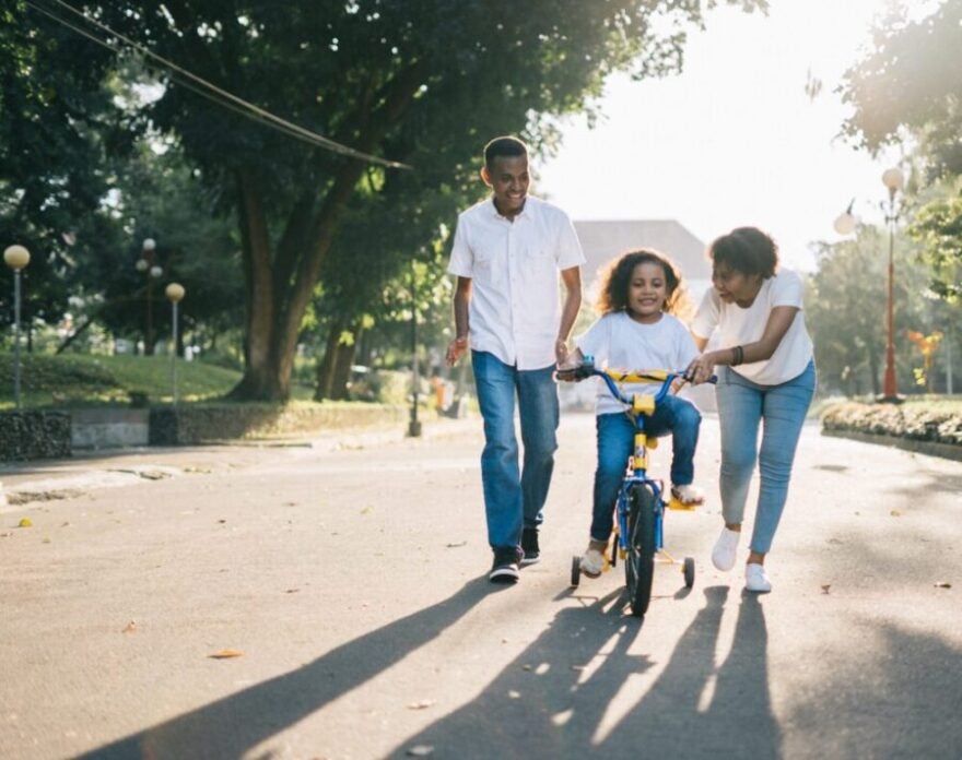 Family teaching child to ride bike with training wheels