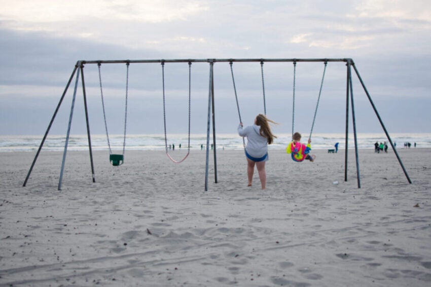 Children swing on a swing set at the beach.