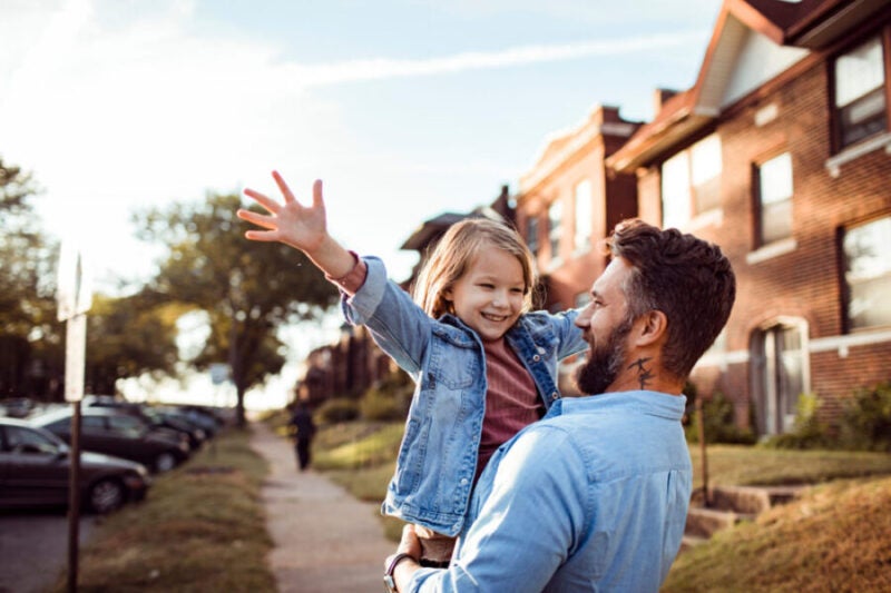 Father and young daughter hugging on a sidewalk of a city,