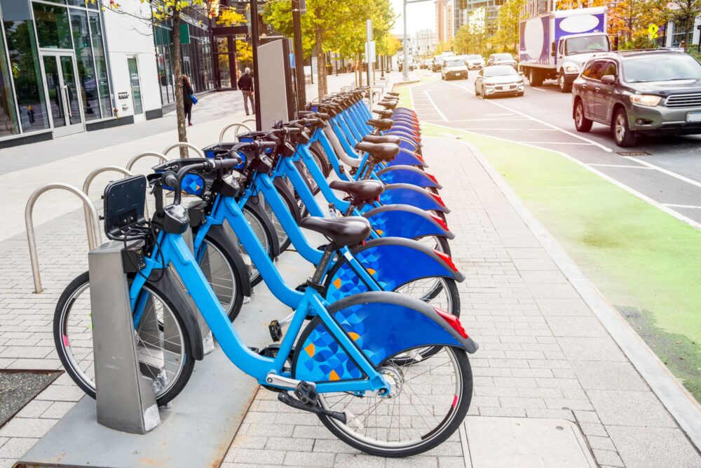Stock image of blue bikes docked at a bike share station on a city street.