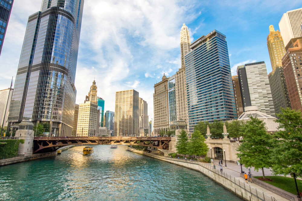 View of the Chicago Riverwalk with a tour boat on the water, surrounded by tall skyscrapers.