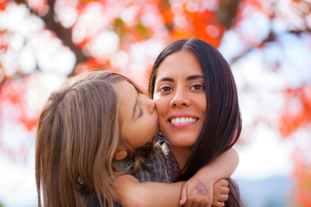 A young girl kisses her mother on the cheek.