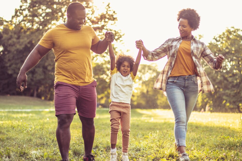 A dad and mom swing their child as they walk together.