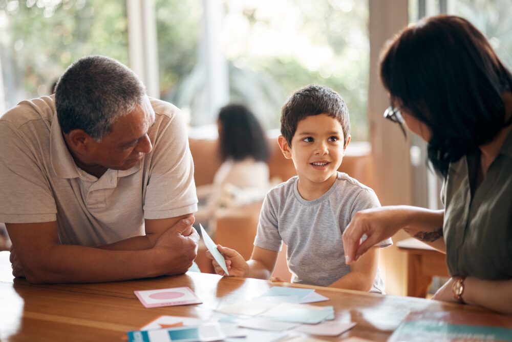 Two adults help a young child with flashcards.