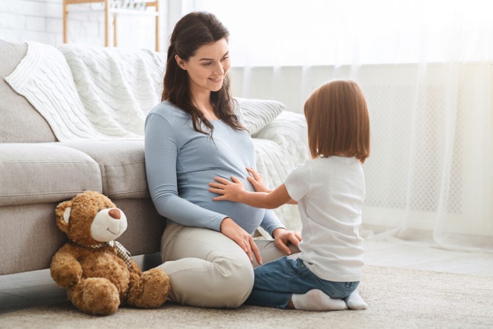 A young baby places her hands on her mother's pregnant stomach.