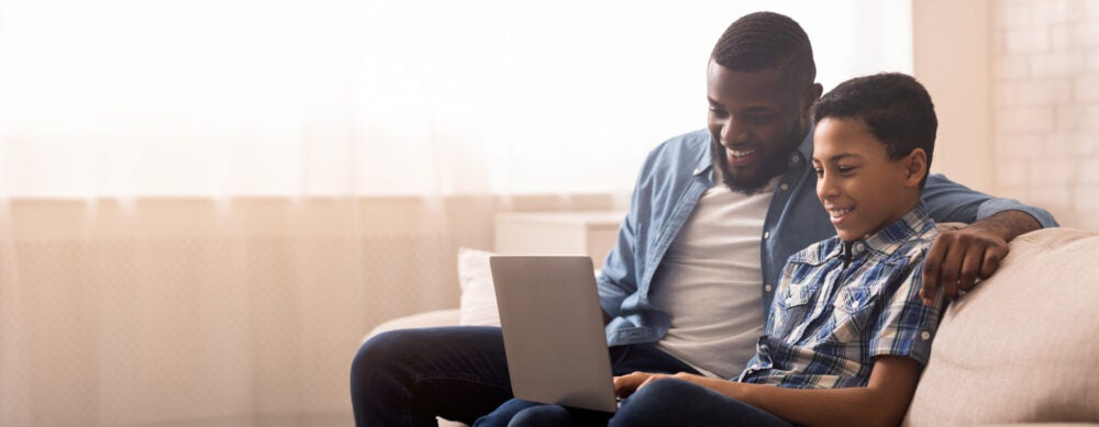 A boy works on a computer with the help of a family member.