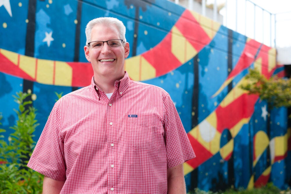 Man in a red shirt standing in front a blue, red and yellow backdrop