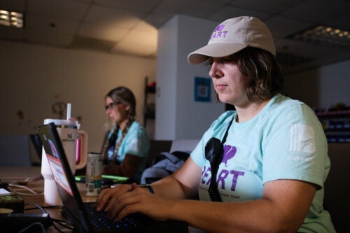 Two women sitting on laptops wearing radios and shirts that say 'HEART'.