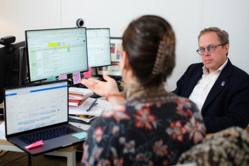 Woman pointing to a computer with a spreadsheet while speaking to a man.