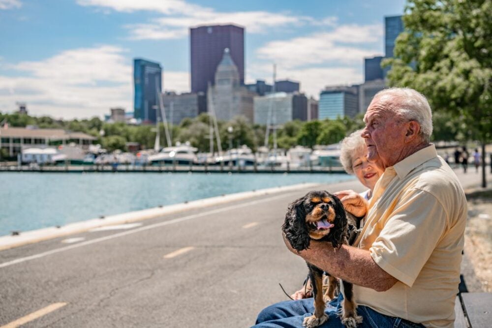 An elderly couple sits outside on a bench along a water walkway in Chicago.