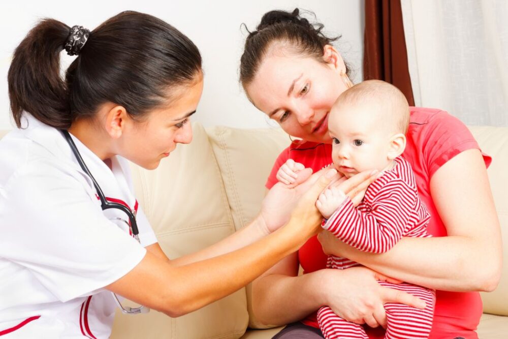 A home visiting nurse checks a young baby being held by his mother.