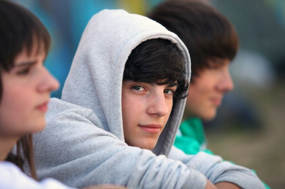 A teenager in a hoodie looks at the camera.